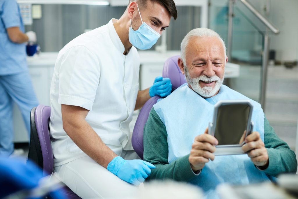 Dentist with a smiling senior patient looking at his new smile in a hand mirror