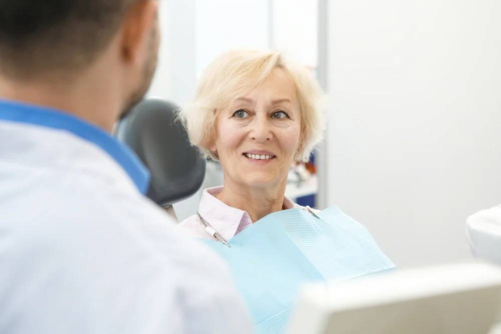 Senior woman with short blonde hair smiling during dental consultation with male dentist in clinical setting